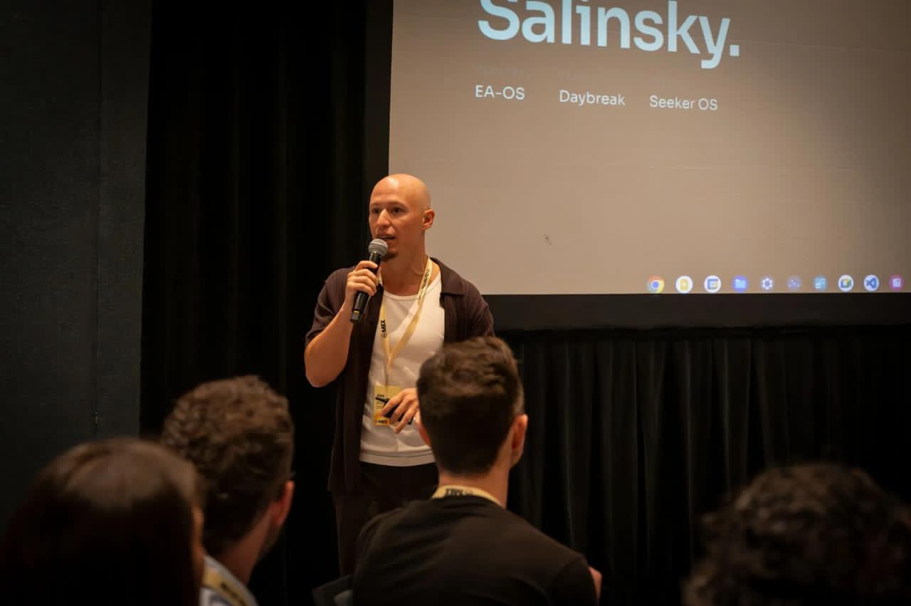 Alex Salinsky presenting on stage with a microphone